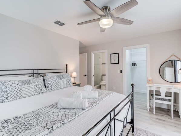 A bedroom with a bed, a desk, a mirror, and a ceiling fan.