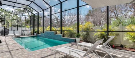 A covered outdoor swimming pool with a view of trees and a clear sky.