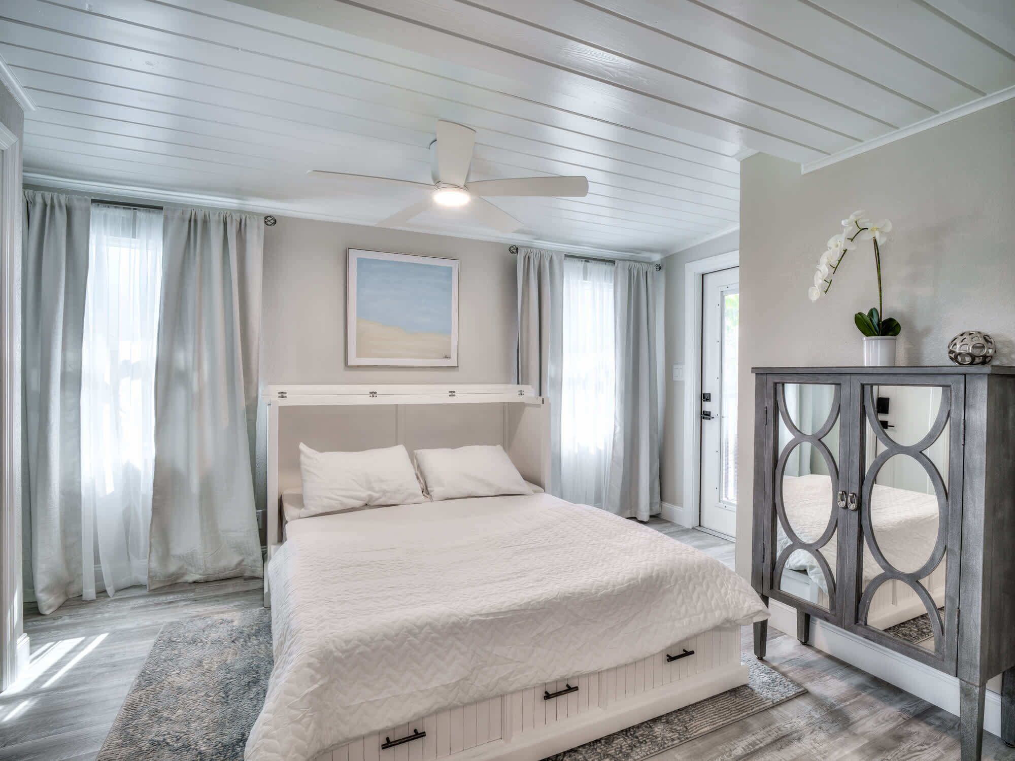 Een slaapkamer met een bed, een plafondventilator, een schilderij, een kast en een potorkidee.
