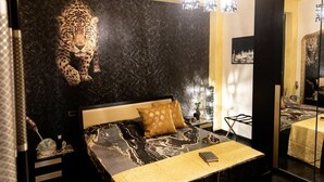 A bedroom with a large mirror, a leopard print headboard, a bedside table with a vase, and a bed with a patterned bedspread. - Dubai RC luxury (Reggio Calabria)