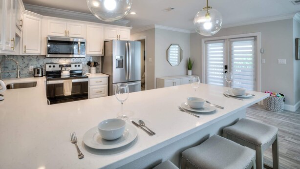 A modern kitchen with white cabinetry, stainless steel appliances, and a central island with bar seating. - Island Gold Steps to the Beach - Heated Pool (Fort Myers Beach)