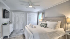 A bedroom with a bed, bedside tables, a ceiling fan, and a door. - Island Gold Steps to the Beach - Heated Pool (Fort Myers Beach)
