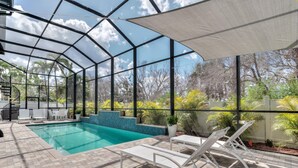 A covered outdoor swimming pool with a view of trees and a clear sky. - Island Gold Steps to the Beach - Heated Pool (Fort Myers Beach)