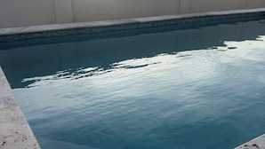 En swimmingpool med kristallklart blått vatten, omgiven av en vit mur och en stenram.
