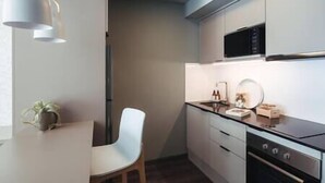 Een moderne keuken met witte kastjes, een zwarte kookplaat en een magnetron. Er staat een witte stoel en een kleine plant op het aanrecht.