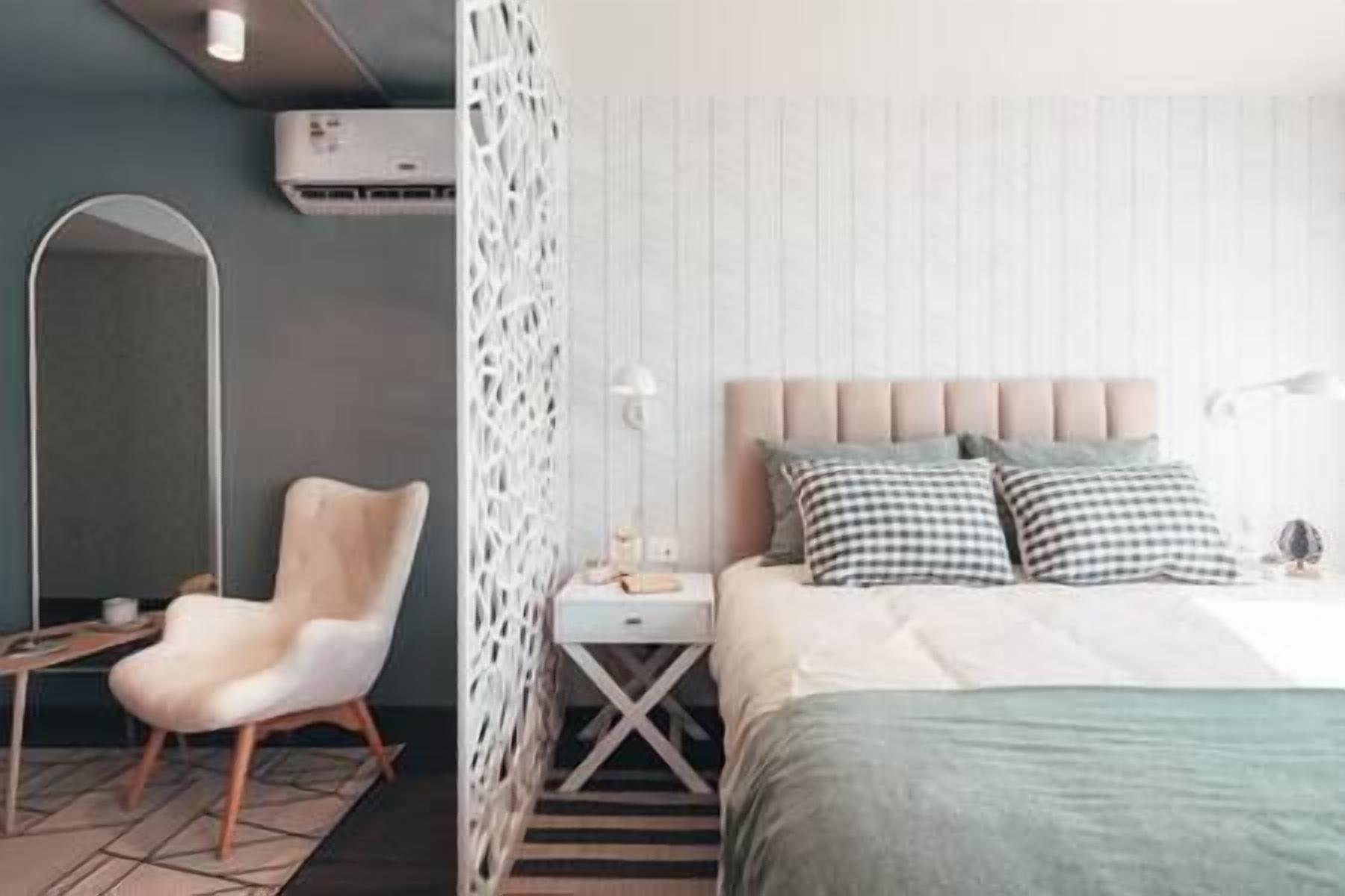 A modern bedroom with a bed, bedside table, chair, and an air conditioning unit.