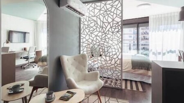 Een moderne woonkamer met een witte fauteuil, een klein rond tafeltje en een decoratieve scheidingswand met een geometrisch patroon.