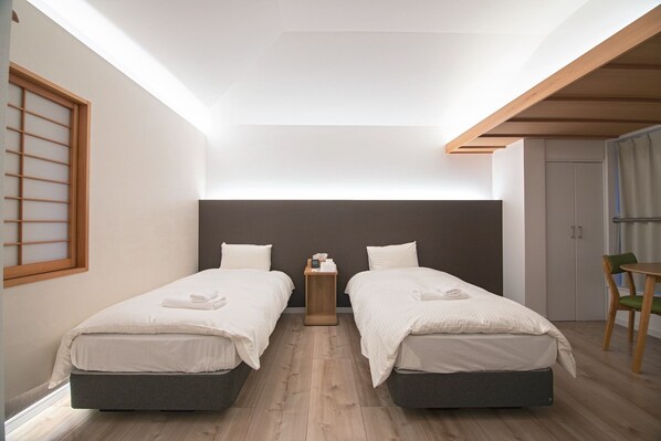 Une chambre d’hôtel moderne avec deux lits, une petite table de chevet en bois, un bureau avec une chaise et un placard à portes coulissantes.
