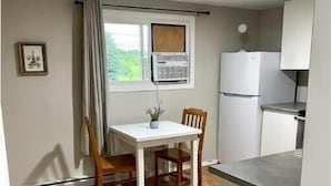 A compact kitchen with a dining table and chairs, a window with curtains, and a refrigerator. - Comfy and modern private suite - everything you need for a short to midterm stay (Dryden)