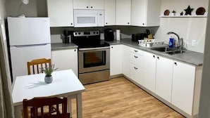 A compact kitchen with white cabinets, a microwave, a stove, a sink, and a dining area with a table and chairs. - Comfy and modern private suite - everything you need for a short to midterm stay (Dryden)