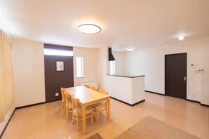 A spacious room with a dining table and chairs, a small kitchenette, and a door.