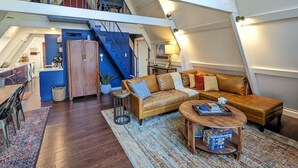 A loft-style living space with a high ceiling, a staircase, a sofa, a coffee table, and a dining area.
