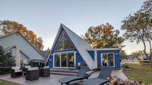A modern house with a blue exterior, a large glass door, and outdoor seating with lounge chairs.