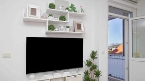 A modern living room with a large flat-screen TV mounted on the wall, surrounded by shelves with decorative items and plants. - MIRROR apartment with parking garage (Dubrovnik)