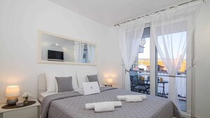 A modern bedroom with a large bed, a bedside table with a lamp, a mirror, and a balcony with outdoor seating. - MIRROR apartment with parking garage (Dubrovnik)