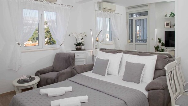 A bedroom with a bed, bedside tables, a chair, and a window with curtains. - MIRROR apartment with parking garage (Dubrovnik)