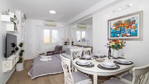 A modern, well-lit room with a dining area, a sofa, and a TV. - MIRROR apartment with parking garage (Dubrovnik)