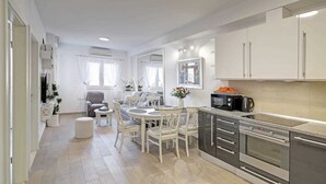 A modern kitchen with a dining area, featuring a central island, white cabinetry, and stainless steel appliances. - MIRROR apartment with parking garage (Dubrovnik)