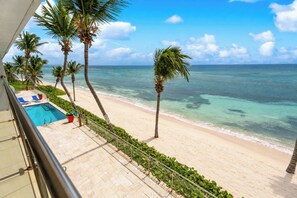 A beachfront property with a pool, palm trees, and a view of the ocean.