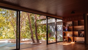 Amplia habitación con grandes puertas correderas de vidrio que dan a un espacio exterior con árboles y una piscina.