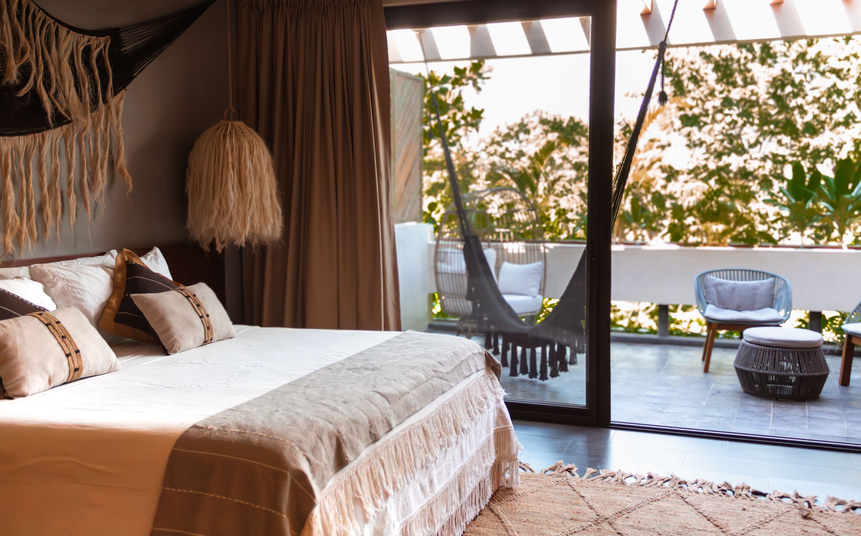 A bedroom with a large bed, a hanging chair, and a view of an outdoor seating area.