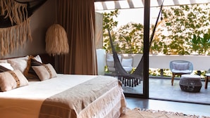 Un dormitorio con una cama grande, una silla colgante y vistas a un área de estar al aire libre.