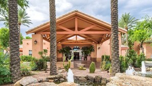 Entrada de hotel com um pátio coberto, palmeiras e um jardim de pedras.