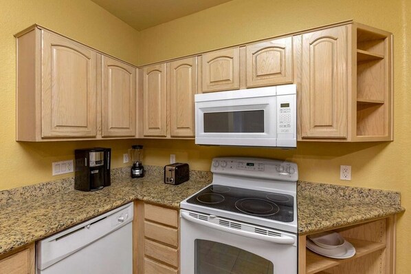 Una cocina compacta con armarios de madera, microondas, estufa, lavavajillas y cafetera.