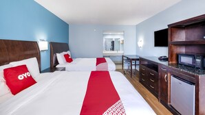 Quarto de hotel com duas camas, uma escrivaninha, micro-ondas e frigorífico.