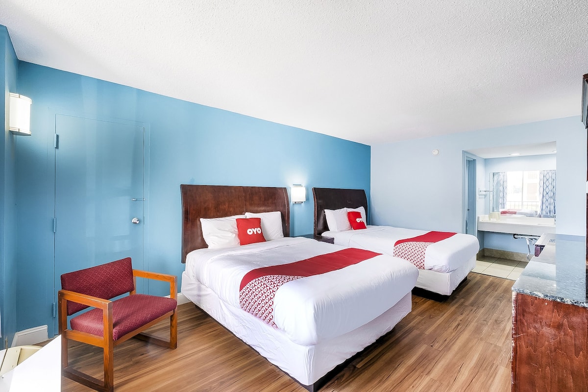 A hotel room with two beds, a wooden chair, a desk, and a bathroom visible through an open door.