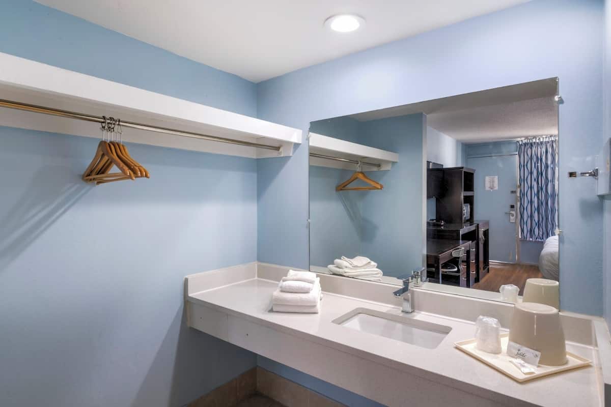A modern bathroom with a large mirror, white countertop, and wooden hangers on a rack.