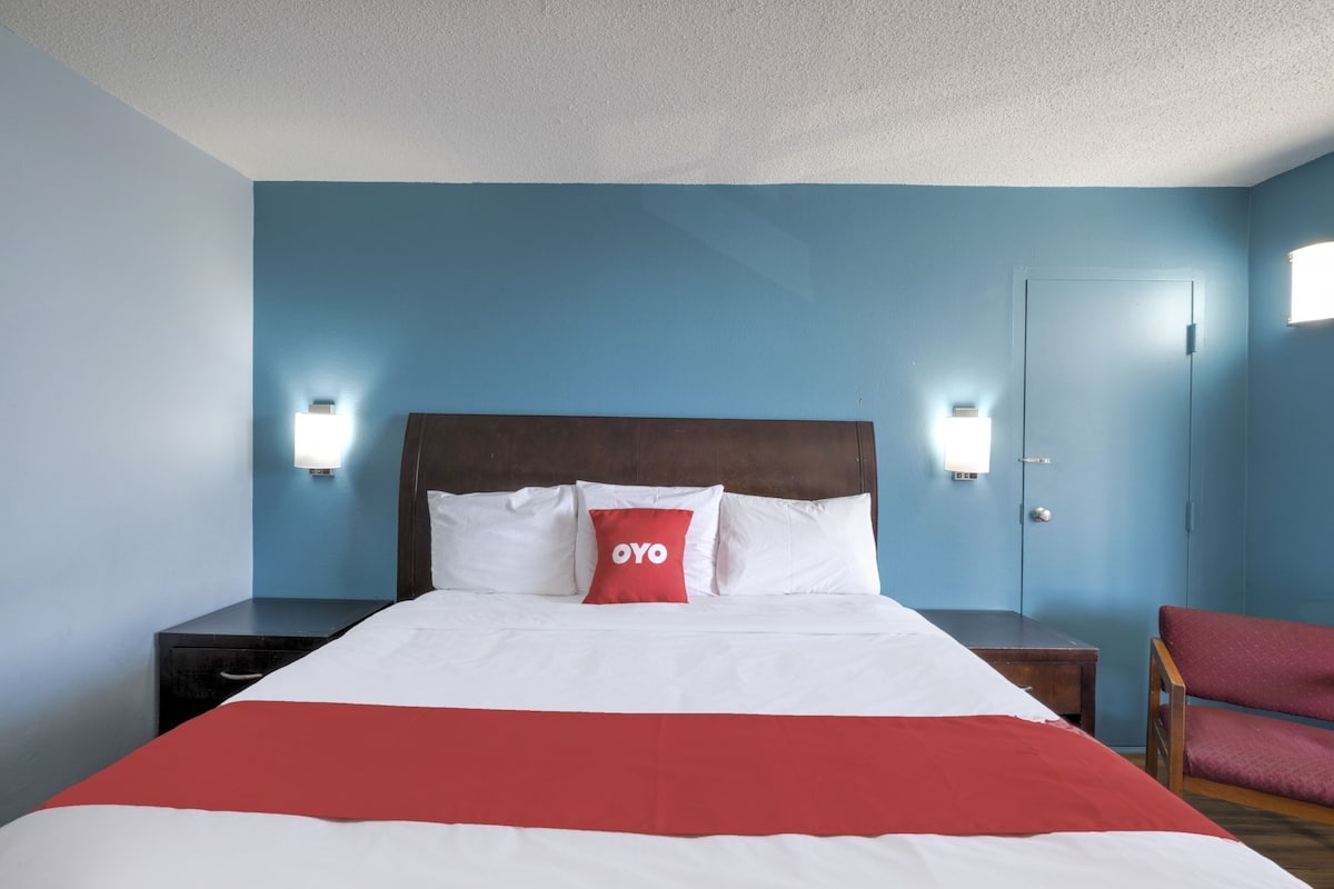 A hotel room with a bed, a nightstand, a chair, and a door.
