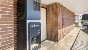 Um dispensador de gelo exterior fixado a uma parede de tijolos, uma porta e uma área de varanda com guarda-corrimão.