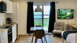 A modern kitchen with a microwave, coffee maker, and dining table. There is a TV mounted on the wall and a sofa in the living area. - Appart-Hôtel L'UNI (Québec City)