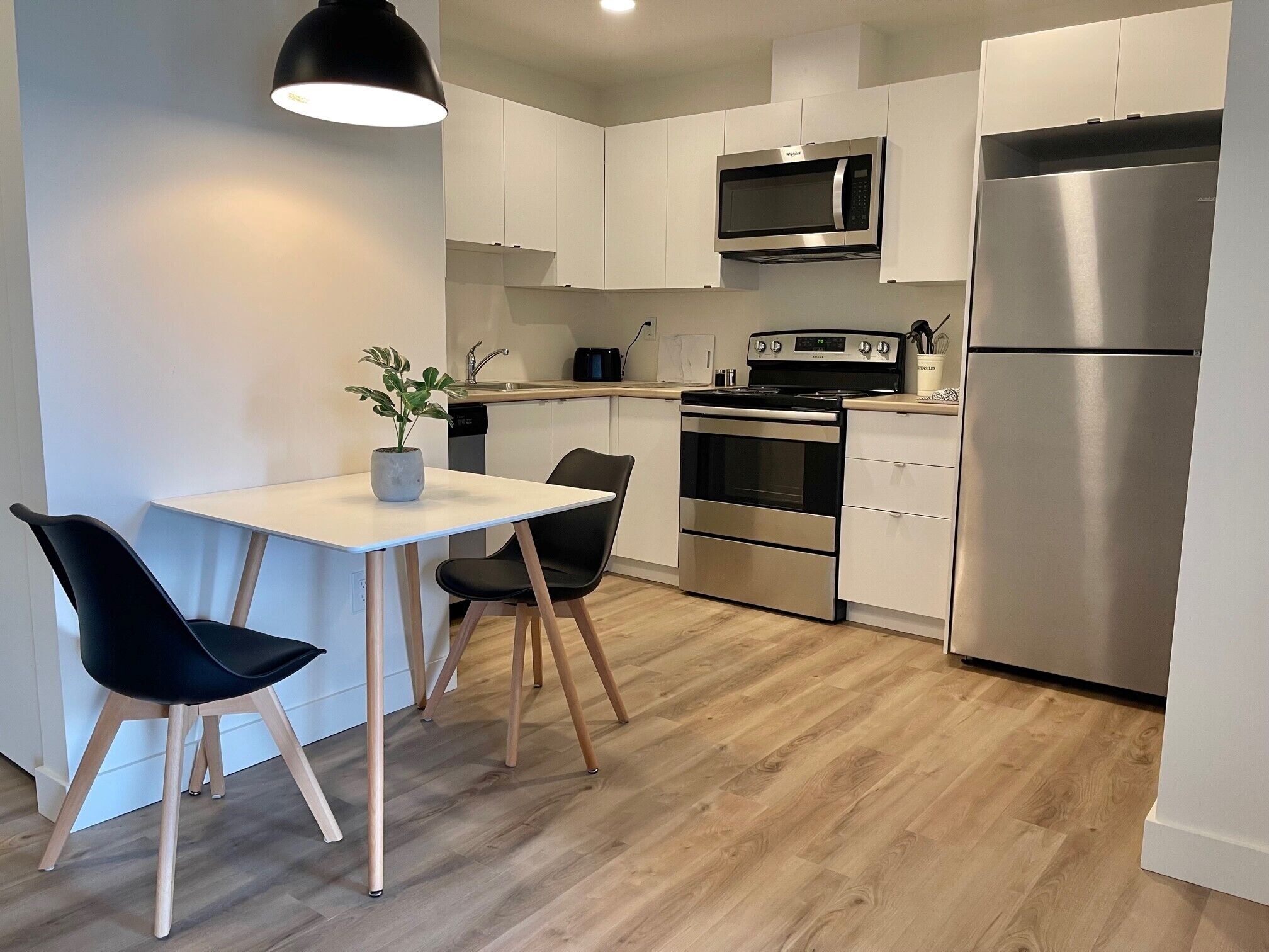 Une cuisine moderne avec des meubles blancs, des appareils en acier inoxydable, une table à manger en bois et des chaises noires.
