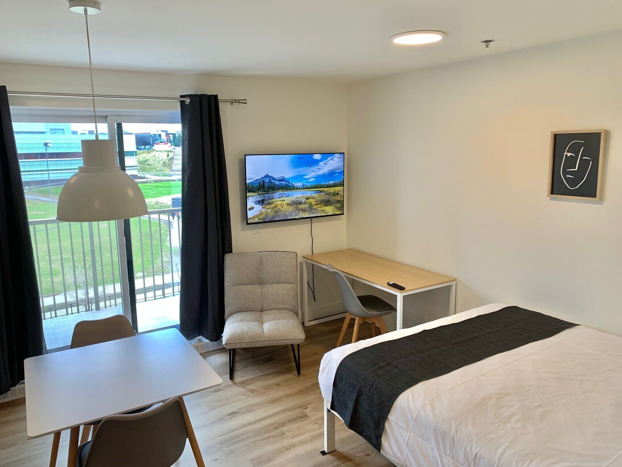 Ein Hotelzimmer mit Bett, Schreibtisch, Stuhl, Fernseher und einem Balkon mit Vorhängen.