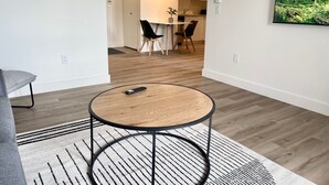 A modern living room with a round wooden coffee table, a grey sofa, and a patterned rug. - Appart-Hôtel L'UNI (Québec City)