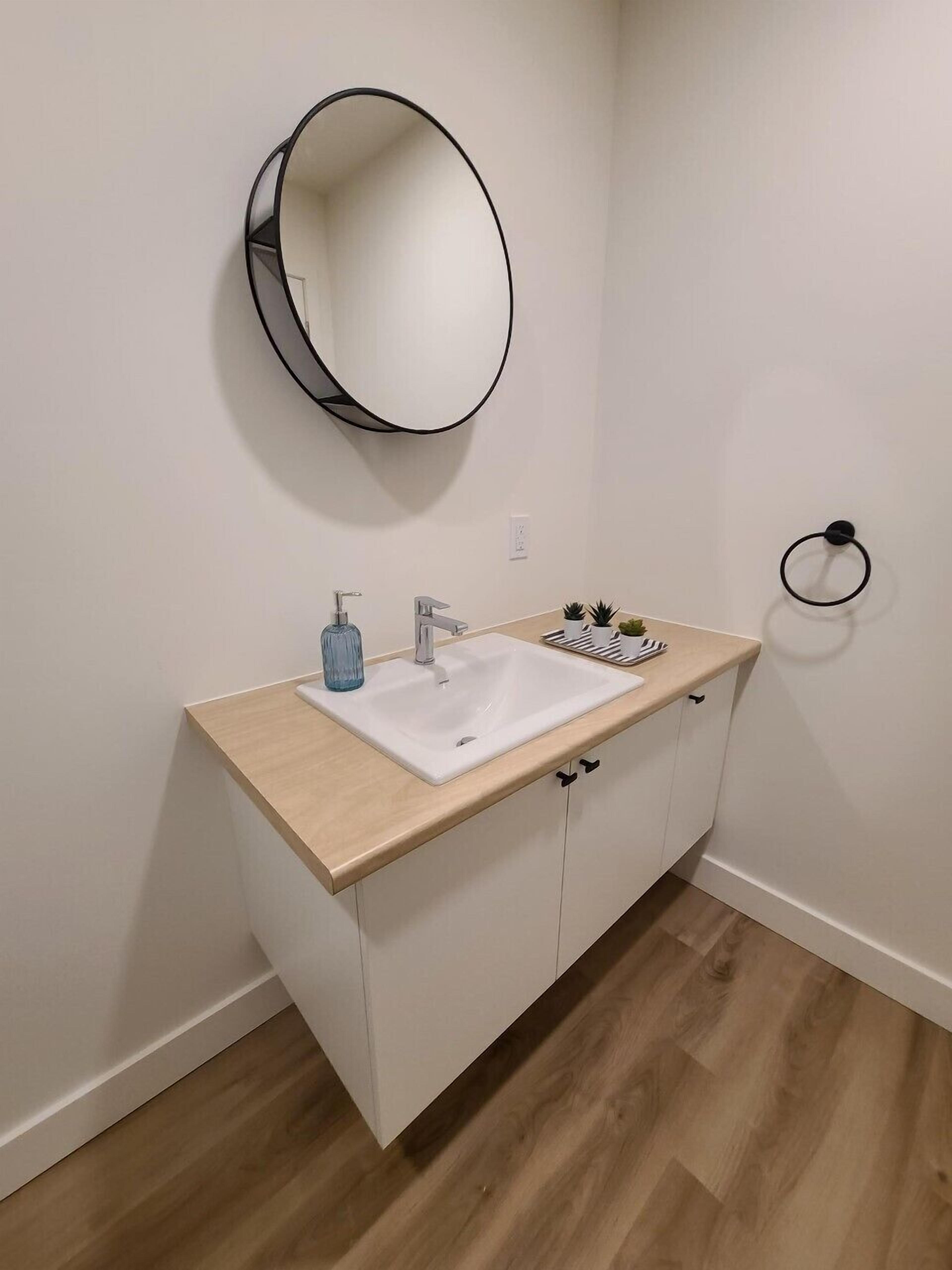 Une salle de bain avec un lavabo blanc, un miroir rond et un plan de toilette en bois.