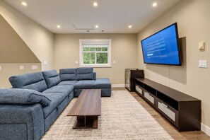 A modern living room with a sectional sofa, a flat-screen TV mounted on the wall, and a wooden coffee table.