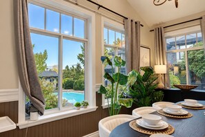 A dining area with a view of a swimming pool, large windows, and a table set with white plates and bowls.