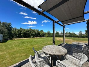 An outdoor patio with a round table and wicker chairs, overlooking a grassy yard and trees. - The River Cabin, Twizel. (Twizel)