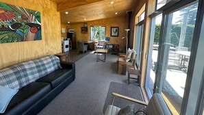 A cozy interior with a wooden ceiling, a black sofa, a dining area, and large windows. - The River Cabin, Twizel. (Twizel)