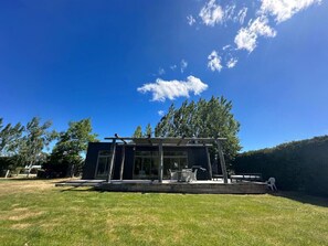 A modern house with a glass facade, a patio with outdoor furniture, and a clear blue sky.