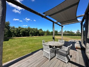 A wooden deck with wicker furniture and a view of a grassy area. - The River Cabin, Twizel. (Twizel)