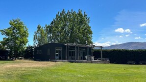 A modern house with a large porch, surrounded by a grassy yard and trees. - The River Cabin, Twizel. (Twizel)