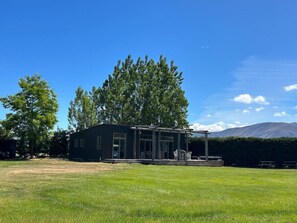A modern house with a large porch, surrounded by a grassy yard and trees.