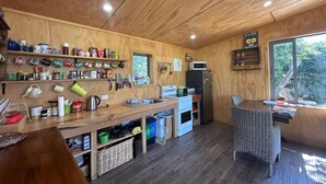 A compact kitchen with wooden walls, a built-in microwave, and a window overlooking greenery. - The River Cabin, Twizel. (Twizel)