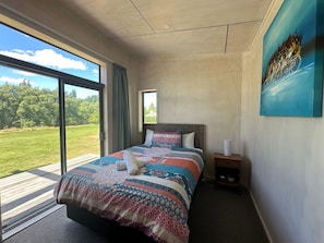 Een slaapkamer met een groot bed, een nachtkastje, een raam met uitzicht op een groen landschap, en een schilderij aan de muur.