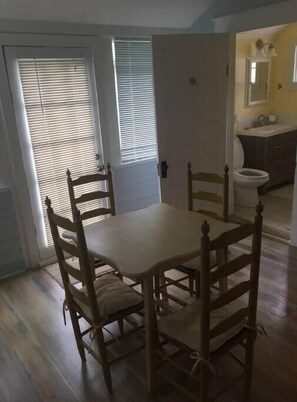 A dining area with a wooden table and four chairs, a white door with blinds, and a kitchen area with a sink and mirror. - Quiet Wilcox County Retreat-Long Leaf Pine Lodge (Rochelle)