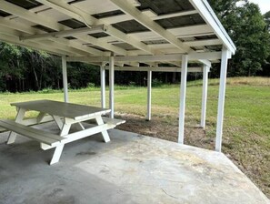 A covered picnic area with a concrete floor and a picnic table. - Harry's House (Rochelle)